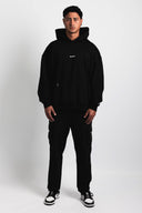 Person wearing a black hoodie and pants with a visible brand logo on a white background